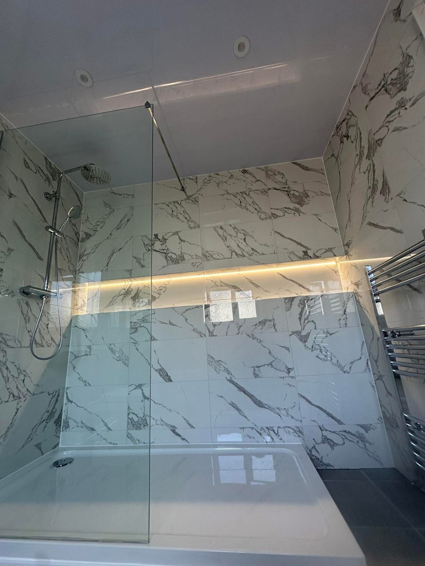 Carrara marble-effect wall tiling in bathroom with LED accent lighting